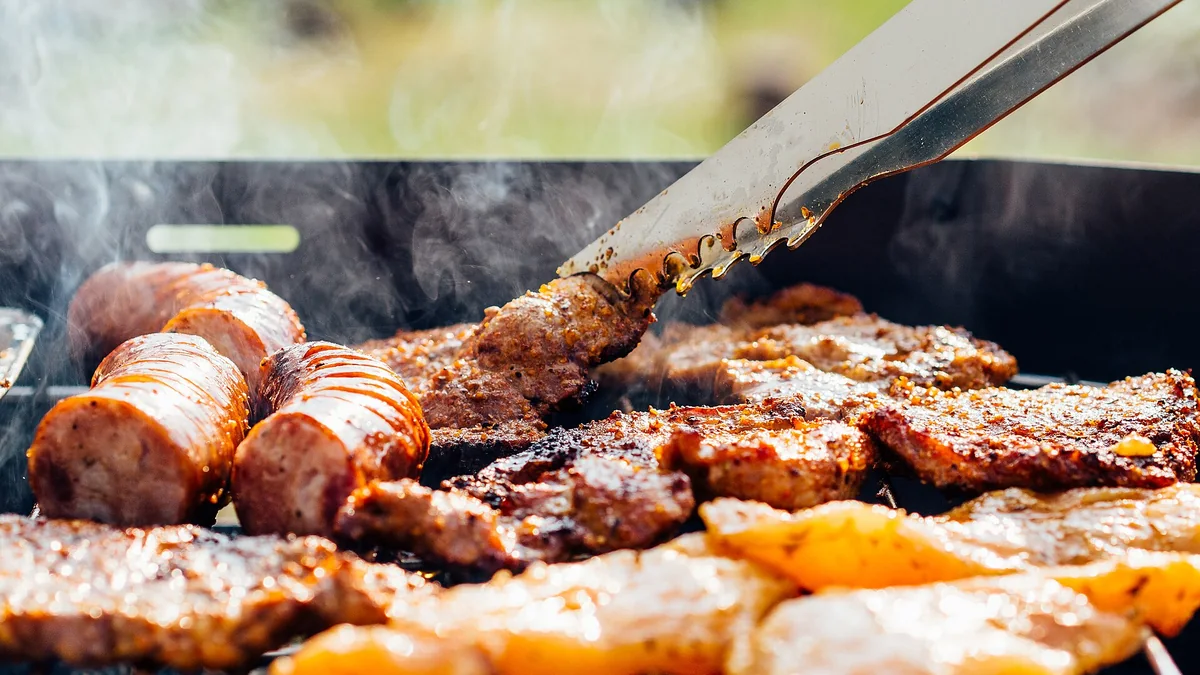 Carne y salchichas cocinándose en la parrilla de una barbacoa al aire libre