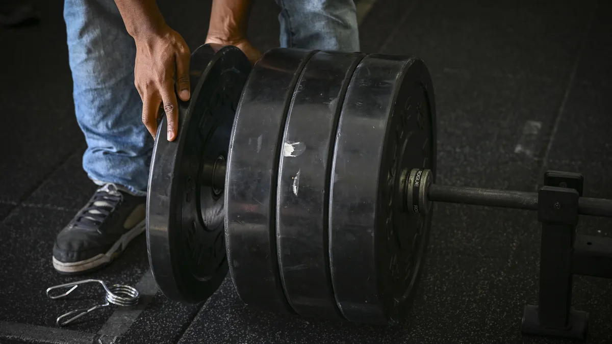 Una persona carga discos en una barra en el suelo de un gimnasio, vista de rodillas para abajo