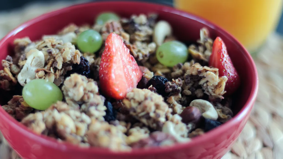 Cuenco de granola con fresas y uvas junto a un vaso de zumo de naranja
