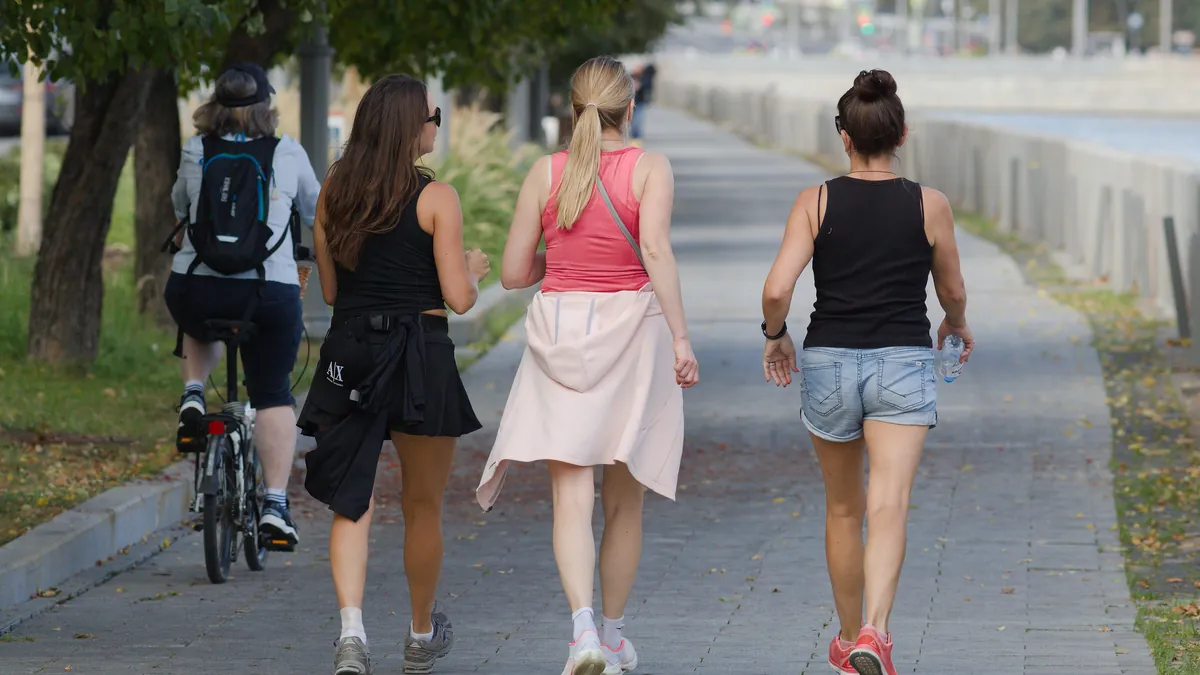 Tres mujeres caminando a paso ligero por un paseo junto al agua, vistas de espaldas