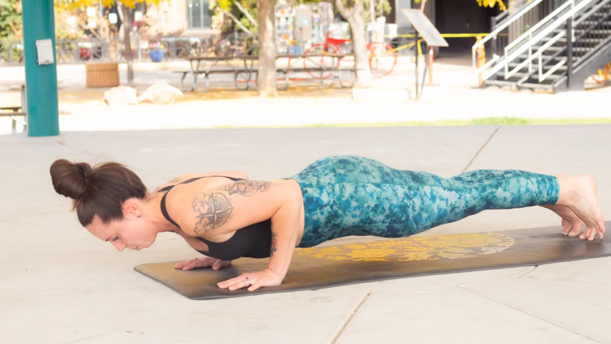 Mujer haciendo una flexión de brazos en posición de plancha sobre una esterilla al aire libre