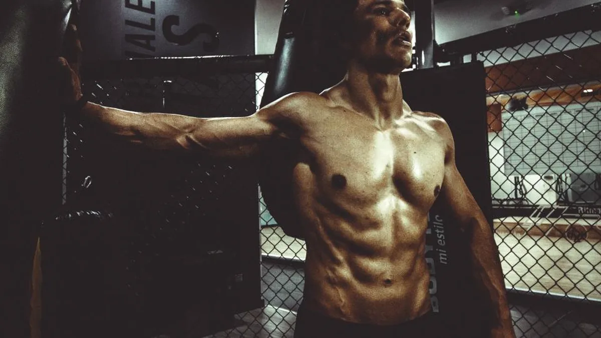 Hombre sin camiseta con el abdomen definido en un gimnasio en penumbra
