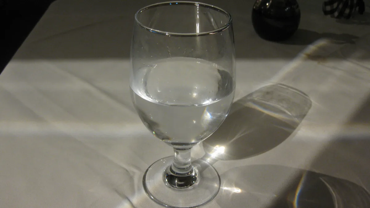 Verre d'eau sur une table à nappe blanche, traversé par la lumière du soleil