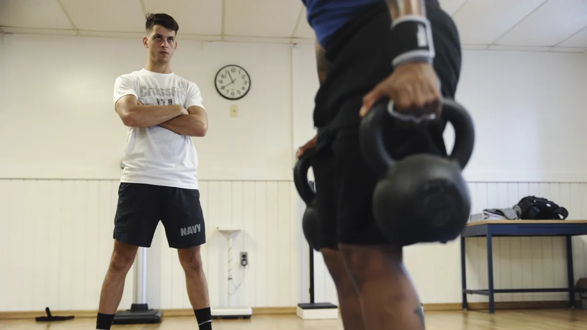 Gym with a wall clock and a person holding a kettlebell in the foreground