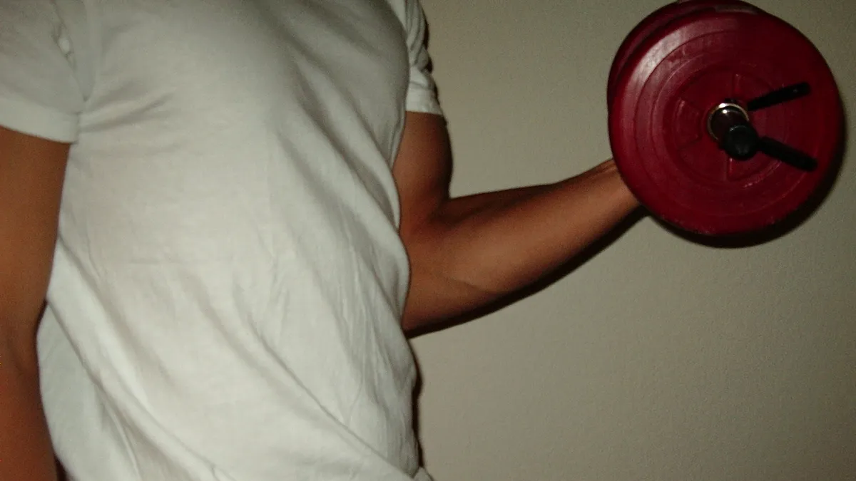 Un hombre con camiseta blanca hace un curl de bíceps con una mancuerna roja