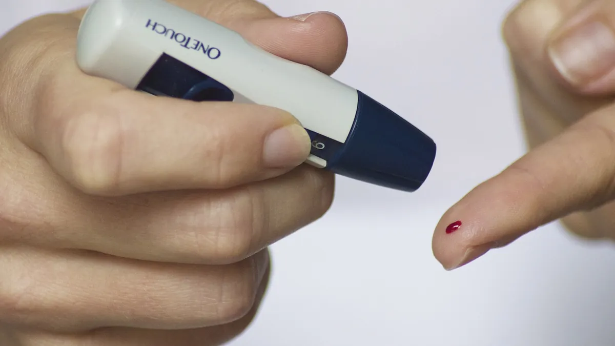Primer plano de una persona pinchándose la yema del dedo con una lanceta para medirse la glucosa