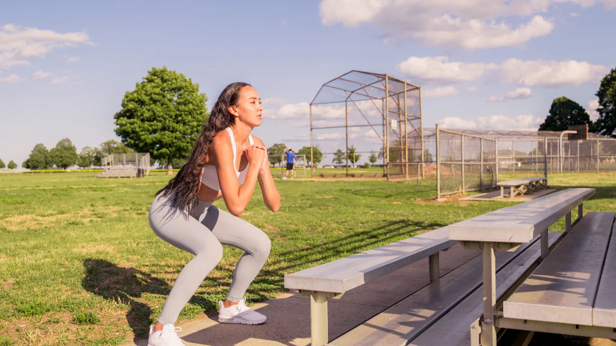 Mujer haciendo una sentadilla al aire libre junto a unas gradas