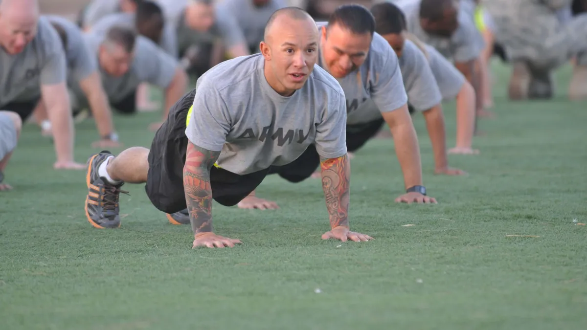 A group of people in grey T-shirts doing push-ups on the grass of a training field