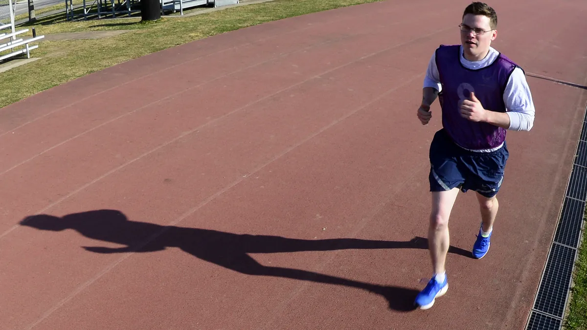 Hombre corriendo por una pista de atletismo con su sombra alargada sobre el tartán