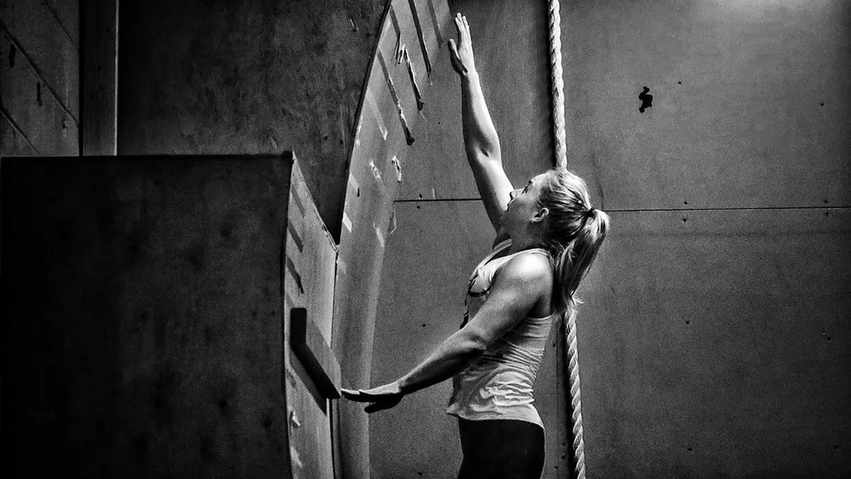 Mujer trepando por una cuerda en un gimnasio, en blanco y negro