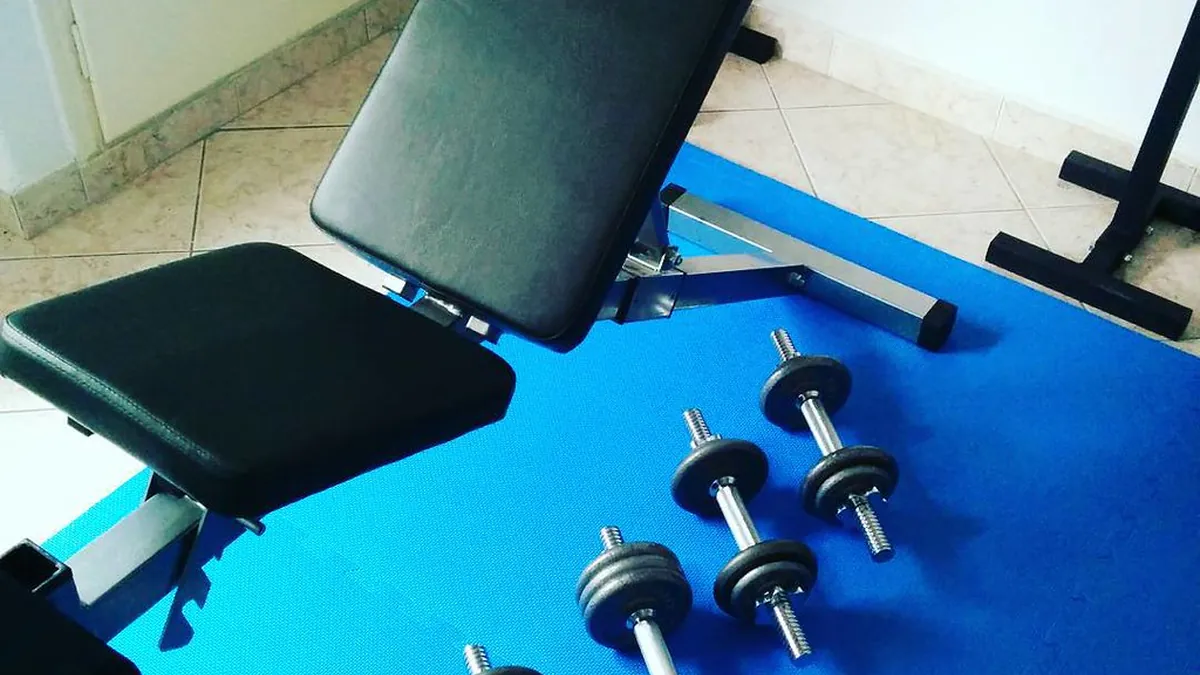 Banco regulable y mancuernas sobre un suelo azul, material para entrenar en casa