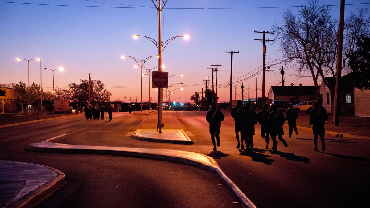 Grupo de personas corriendo por una avenida al amanecer bajo las farolas encendidas