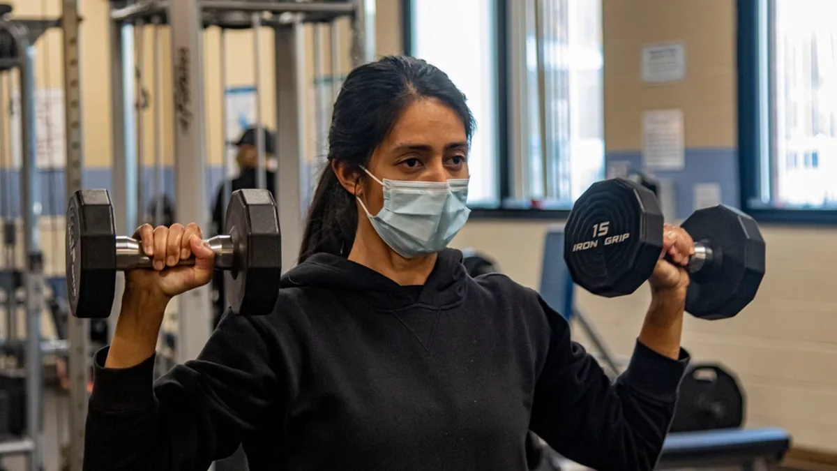 Mujer haciendo press de hombros con mancuernas en un gimnasio