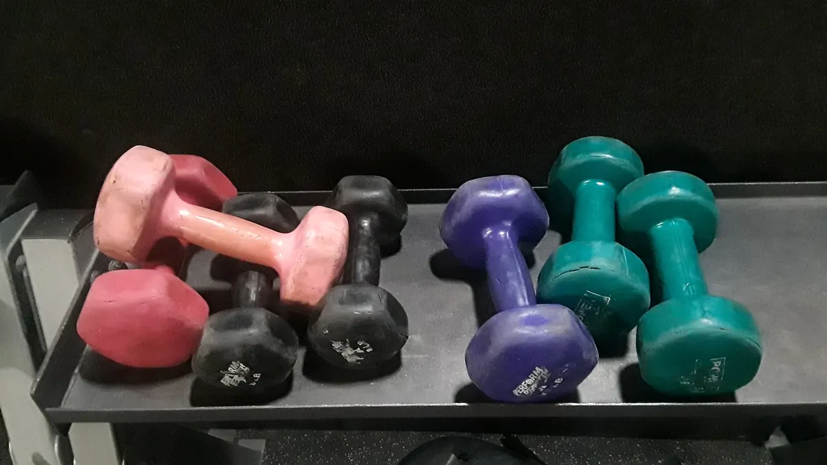 Haltères légers roses, violets et verts sur une étagère de salle de sport