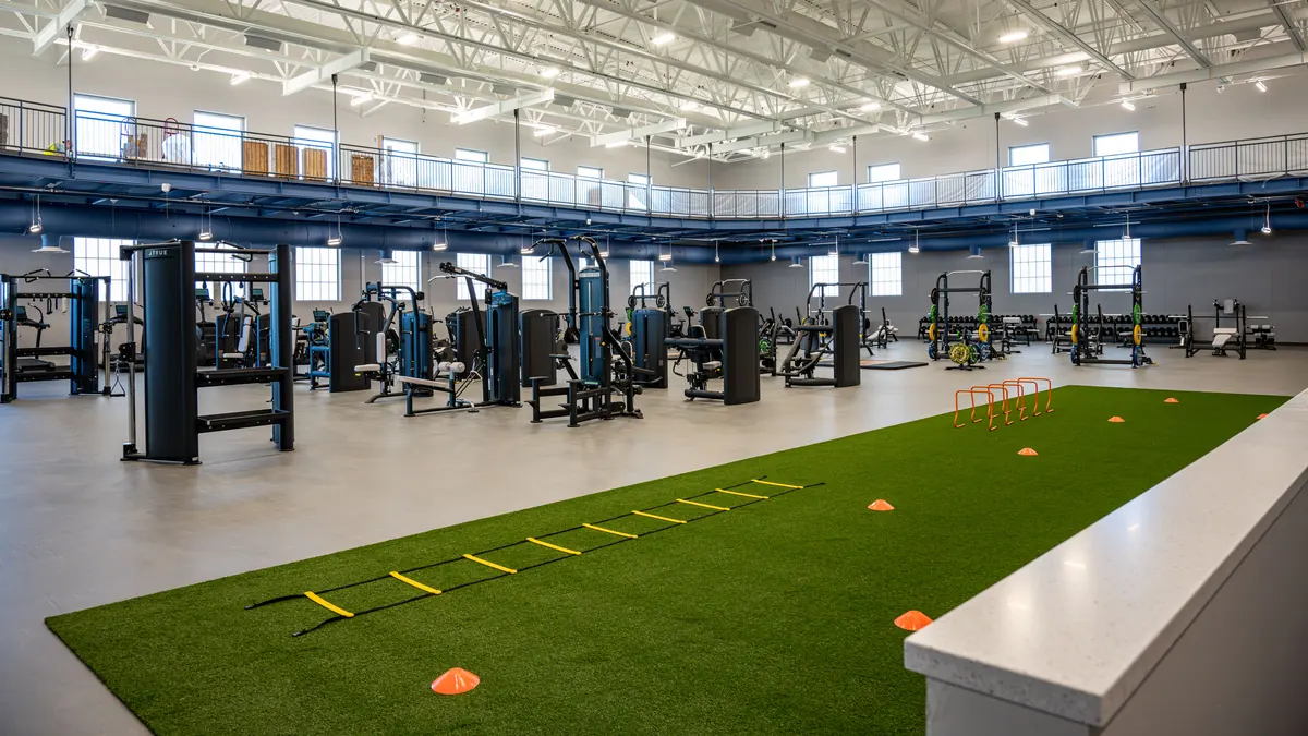 Zona de entrenamiento con césped artificial, escalera de agilidad y conos en un gimnasio amplio