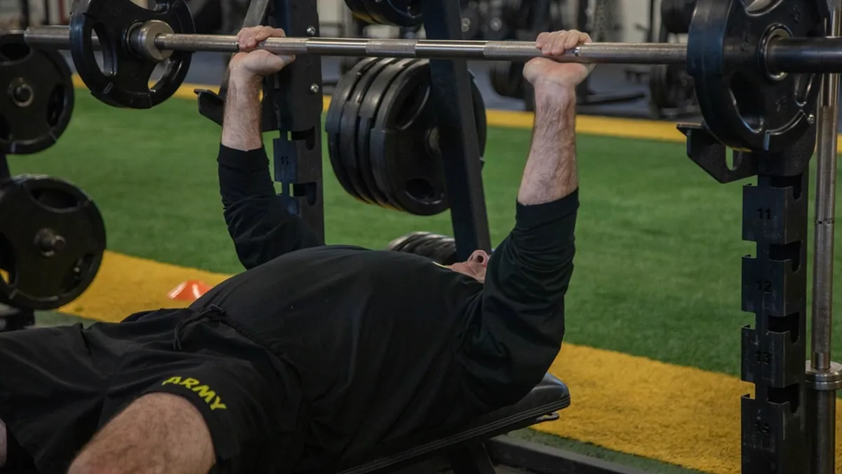 Hombre haciendo press de banca con barra en un gimnasio con césped artificial