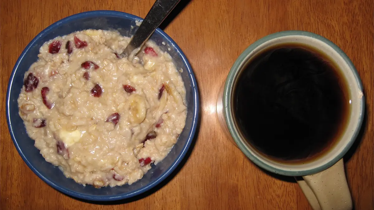 Cuenco de avena con arándanos rojos y plátano junto a una taza de café solo