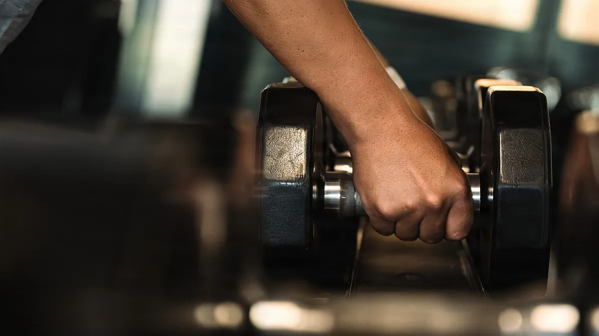 Mano cogiendo una mancuerna del estante de un gimnasio