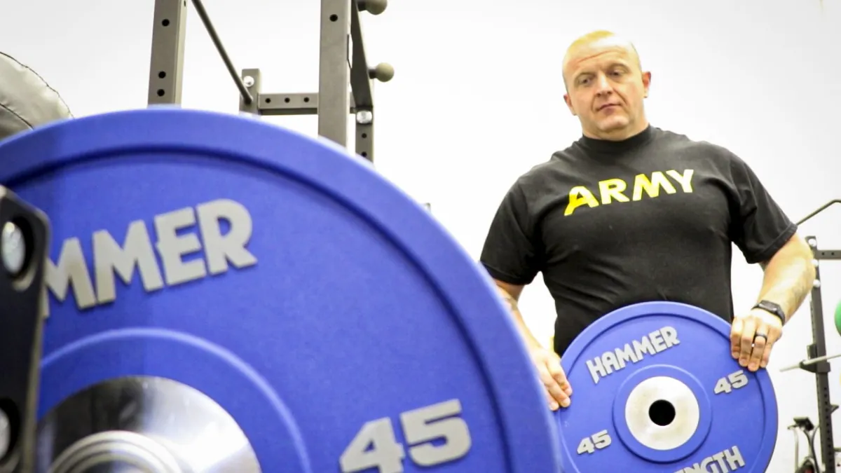 Hombre con un disco en la mano junto a una barra cargada en el gimnasio