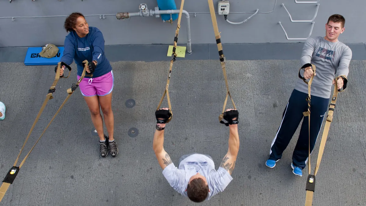 Three people training with suspension straps on a deck, seen from above