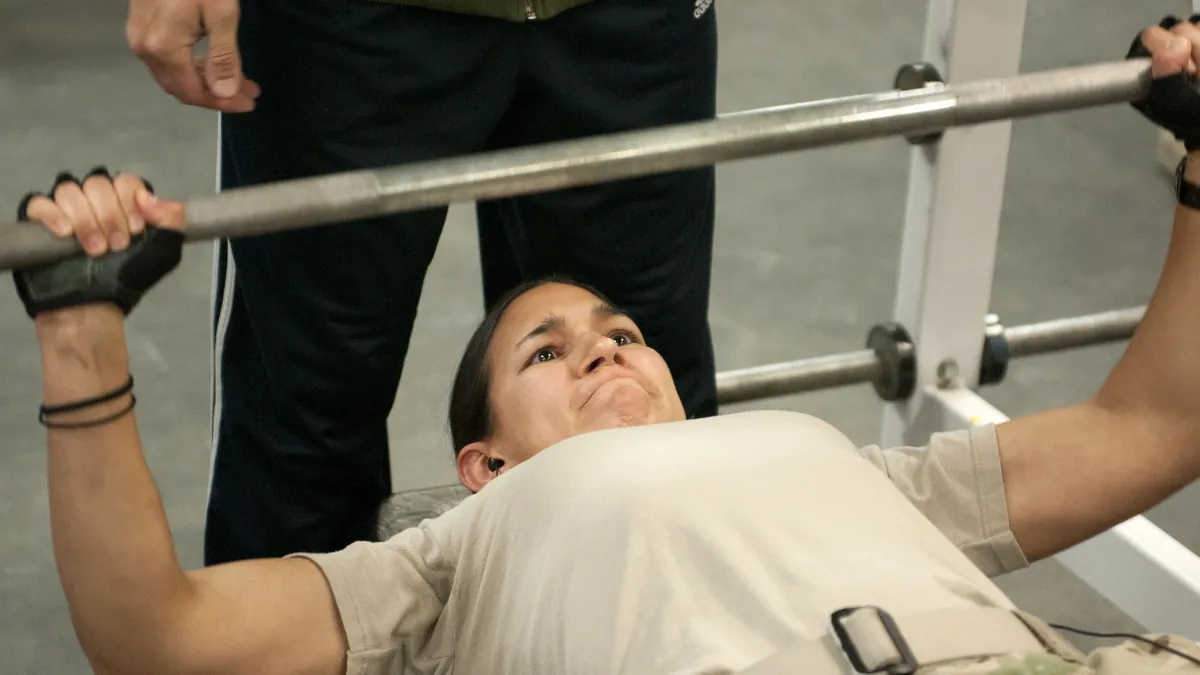 Femme faisant un développé couché à la barre pendant qu'un partenaire l'assure derrière le banc